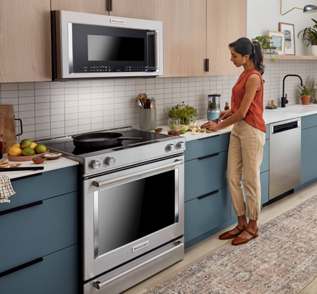 A person cutting up fruits in a modern kitchen that features a suite of KitchenAid® major appliances.