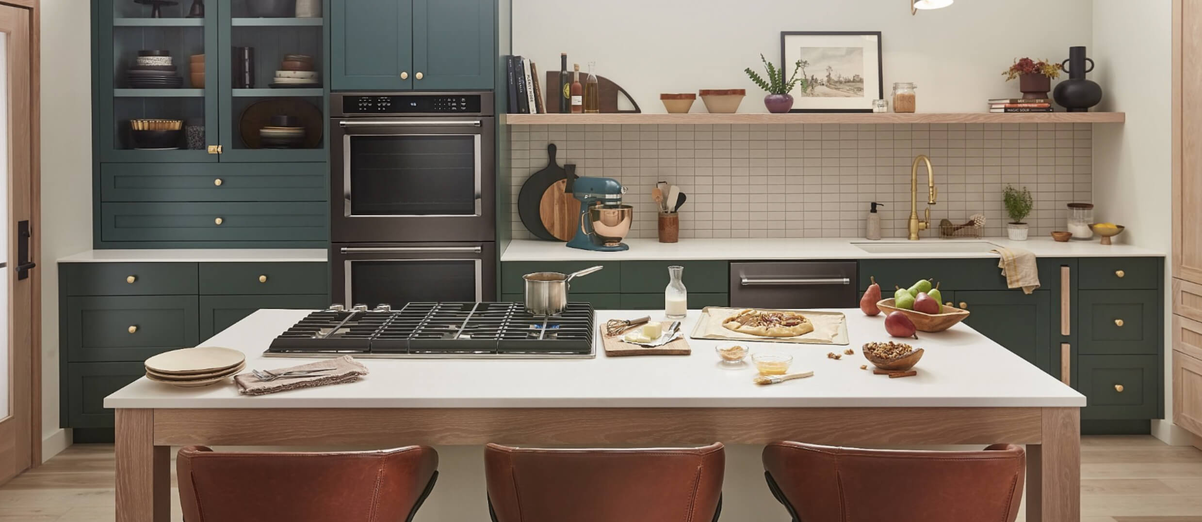 A modern, stylish kitchen with dark green cabinets and different ingredients that features a suite of KitchenAid® appliances.