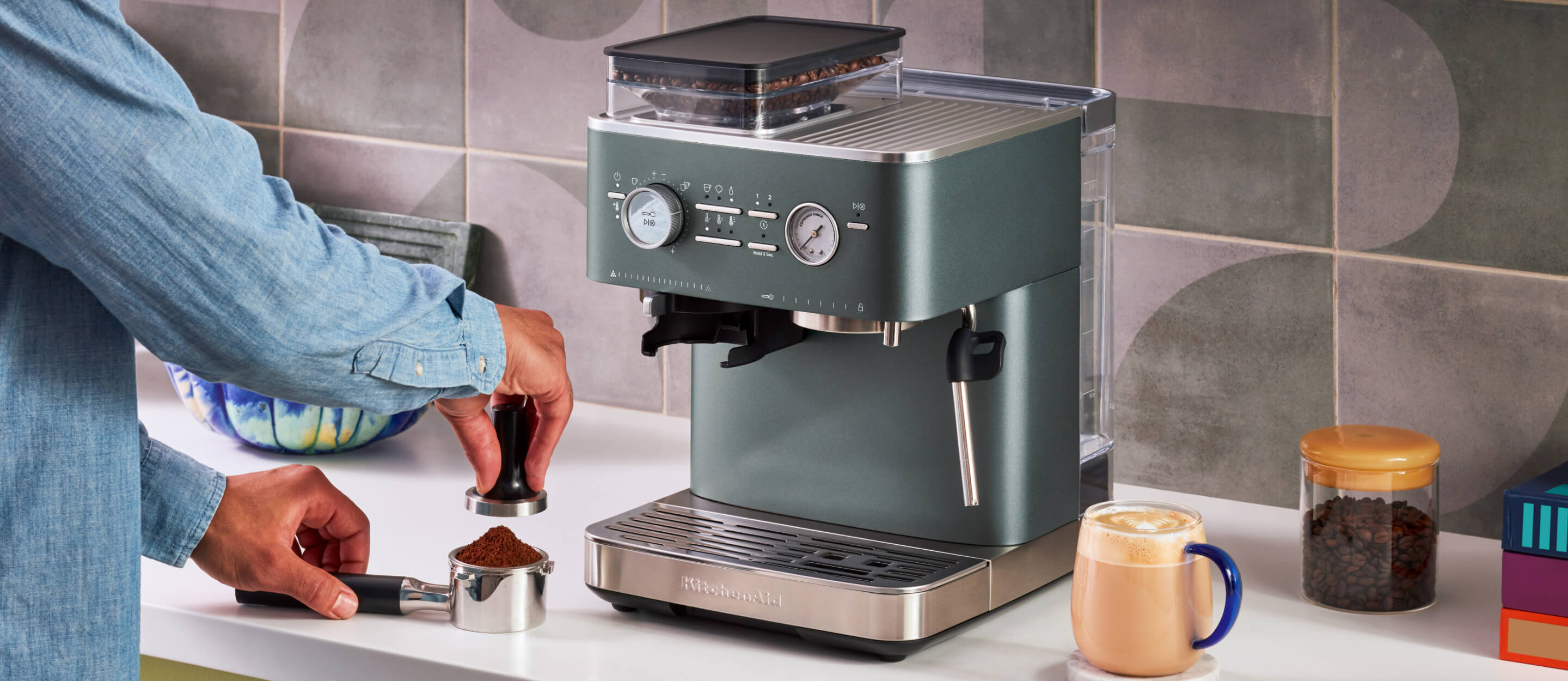 A KitchenAid® espresso machine in juniper, with a person tamping down espresso grounds.