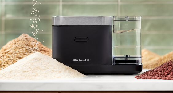A closed grain and rice cooker with small mountains of rice and grains surrounding it.