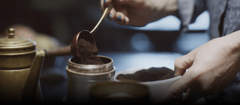 A person adding ground coffee into a bowl.