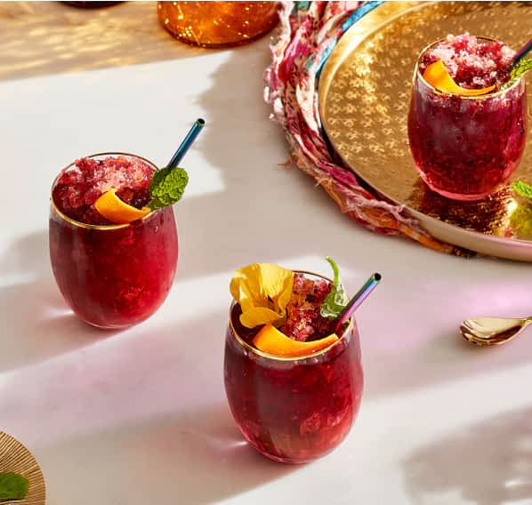 Hibiscus-infused beverages on a countertop, garnished with fried herbs and fruits.