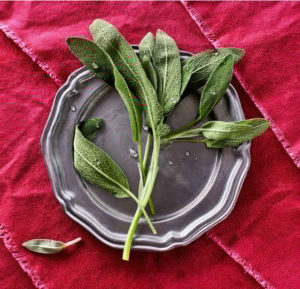 A silver plate of sage on top of a fuchsia tablecloth.