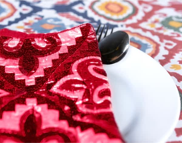 A place setting on a bold table cloth with a fuchsia napkin in a vivid print.