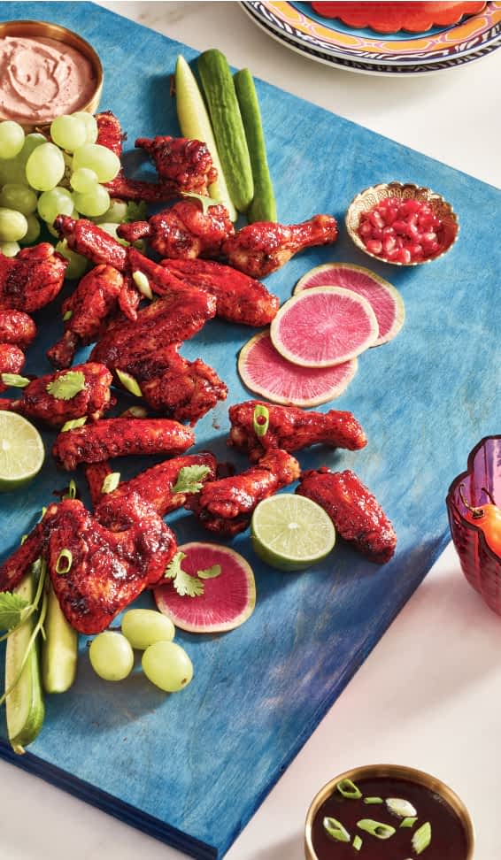 Hibiscus-coated chicken wings on a serving board, with different fruit, vegetable and herb garnishes.