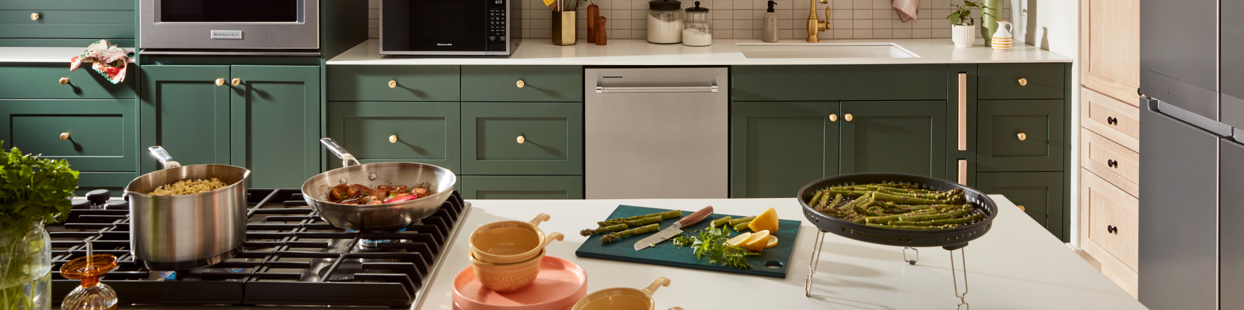 Various food items being cooked on a KitchenAid® rangetop and on the counter of an island. 