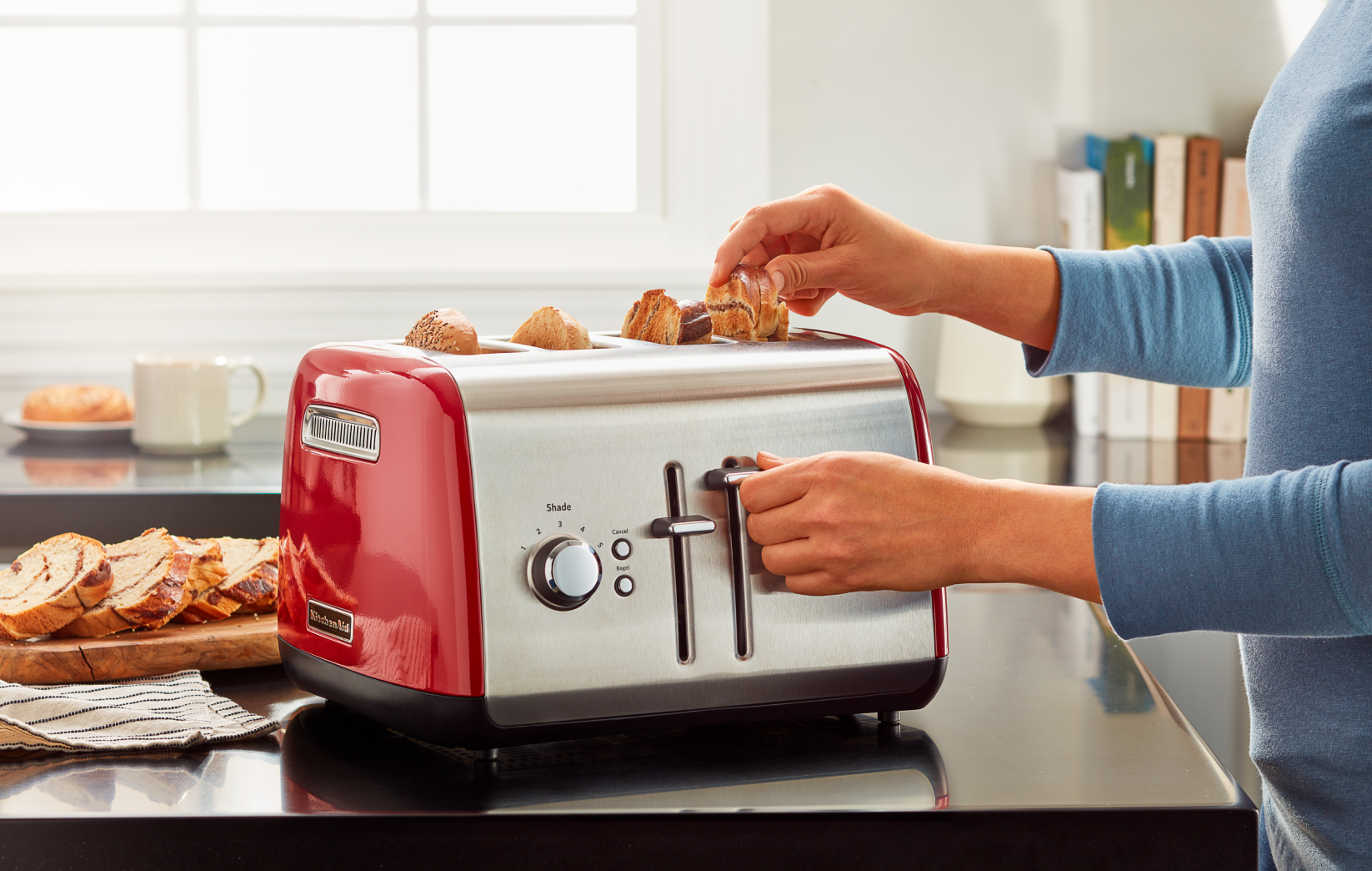 A person toasting bread and bagels in a KitchenAid® 4-Slice Toaster.