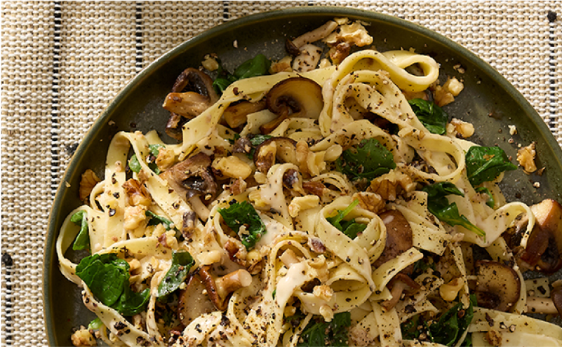 A plate of fresh fettuccine with mushrooms, greens and walnuts.