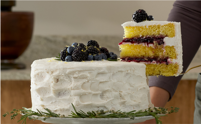 A slice being lifted from a lemon rosemary cake topped with dark berries.