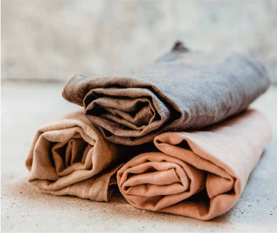 Three rolled up linen hand towels in warm neutral colors.