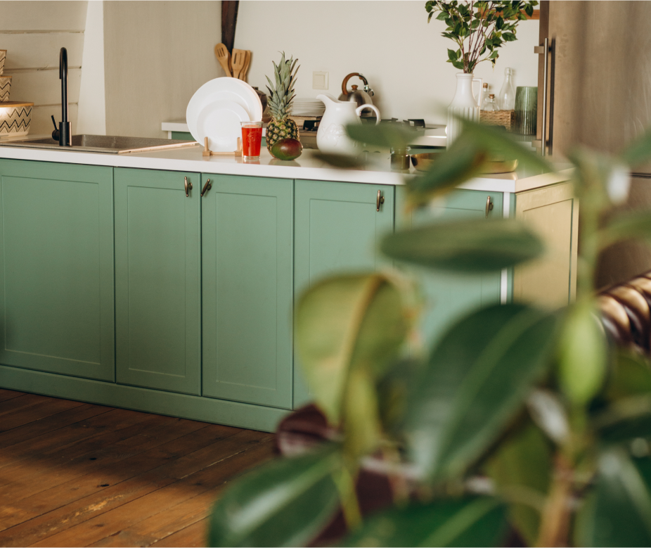 A sage green kitchen with foliage in the foreground.