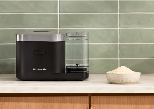A KitchenAid® Grain and Rice Cooker on a white countertop, behind it a green backsplash.
