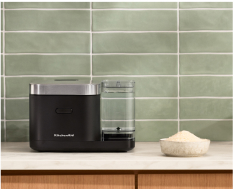 A KitchenAid® Grain and Rice Cooker on a white countertop, behind it a green backsplash.