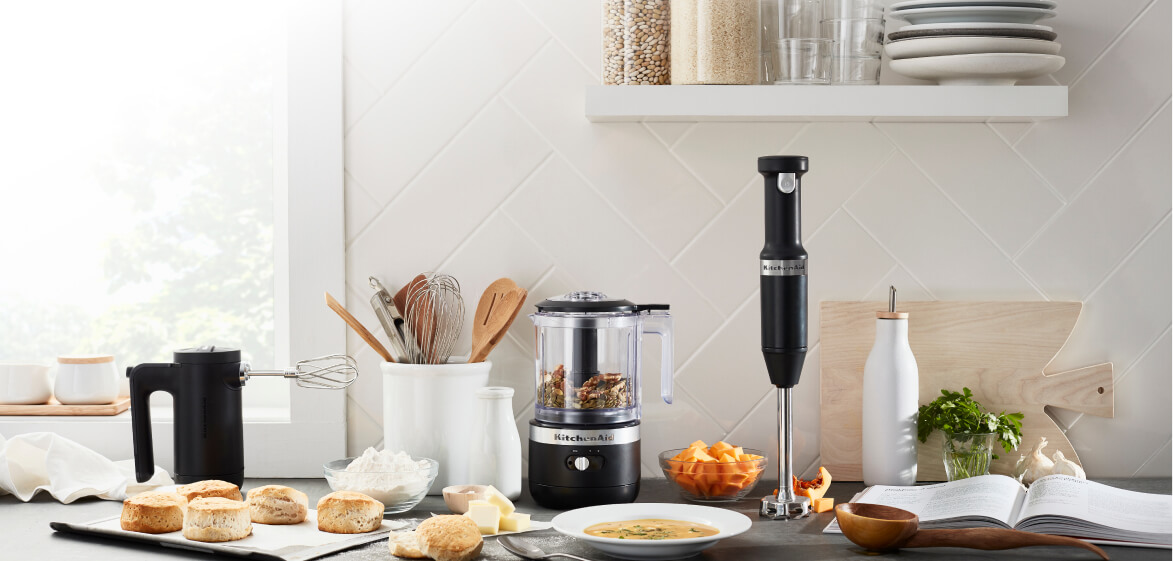 A sun-filled countertop featuring the Matte Black Cordless Chopper, Hand Mixer and Hand Blender.