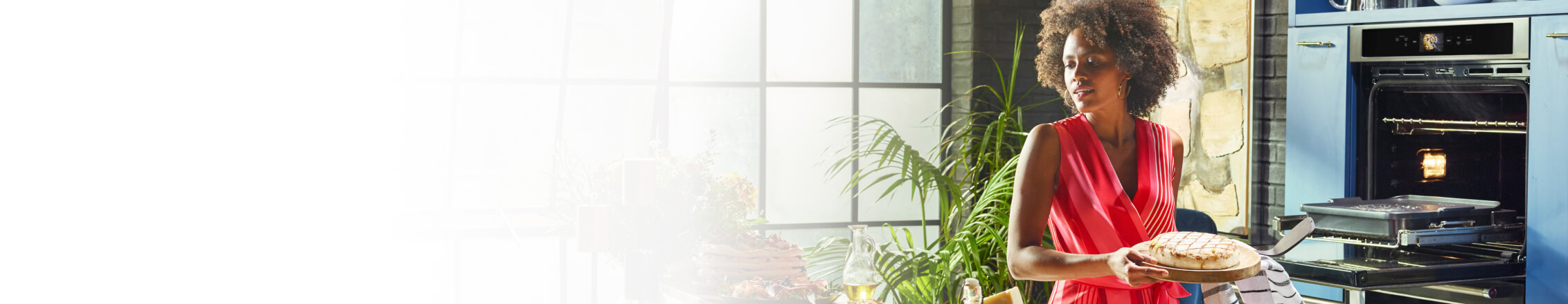 A young woman holding a wooden plate with freshly made bread from her KitchenAid® Smart Oven+.