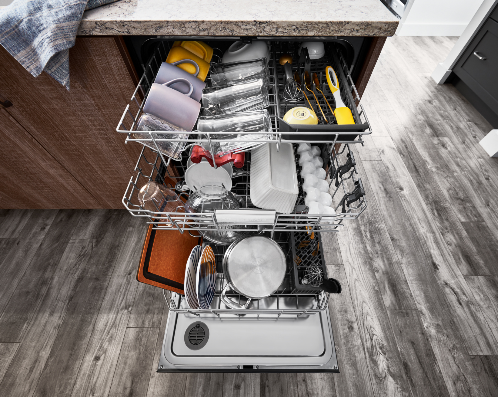 An open KitchenAid® dishwasher, with all racks full of dishware, glassware and utensils.