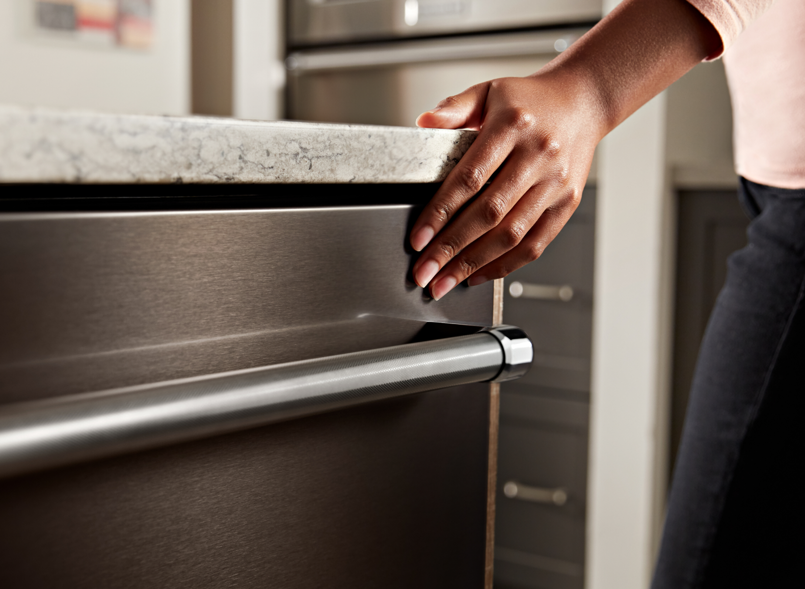 A person touching the exterior of a dishwasher.