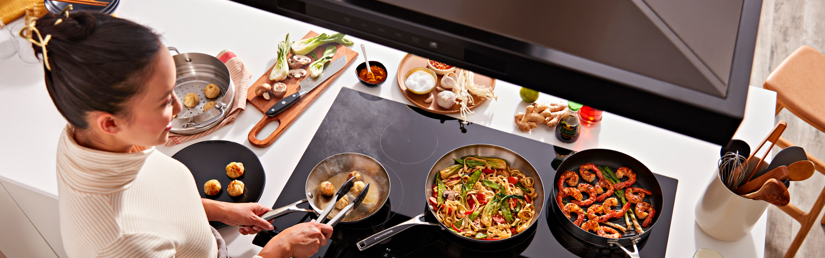 A person cooking on a KitchenAid® cooktop.