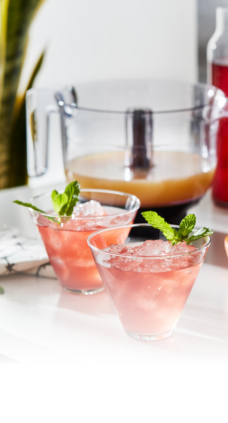 Two freshly made grapefruit cocktails resting on a bright kitchen counter with assorted citruses.