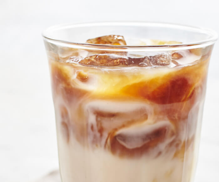 A cold glass of homemade iced coffee next two a small clear, bowl of caramel syrup.