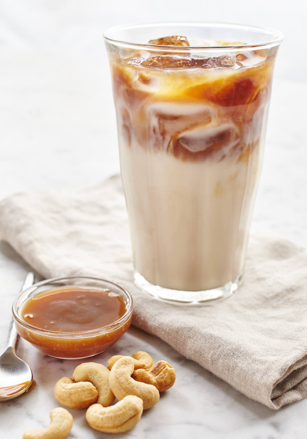 A cold glass of homemade iced coffee next two a small clear, bowl of caramel syrup.