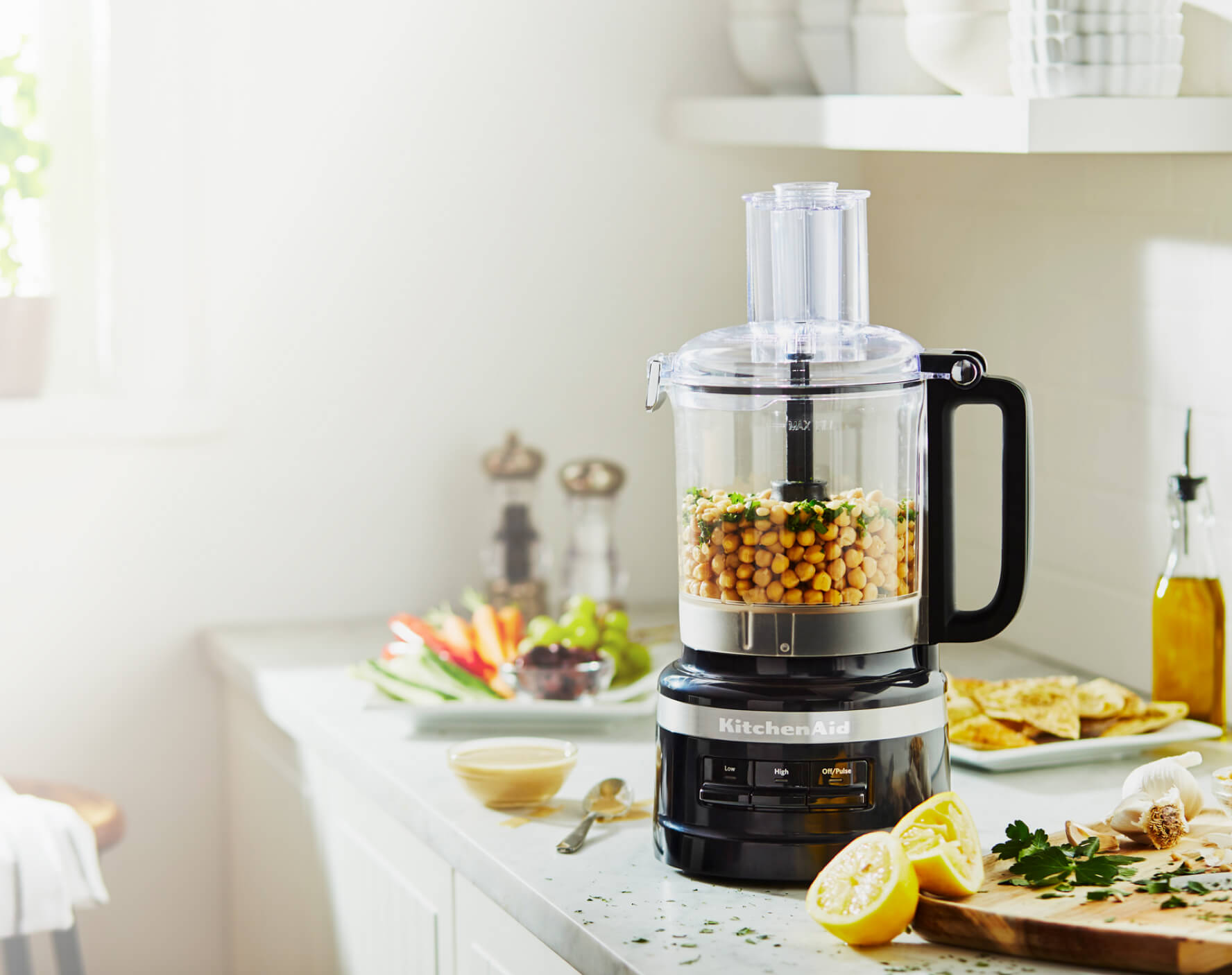 A Black Food Processor with chick peas and cilantro resting next to sliced lemons and other produce.