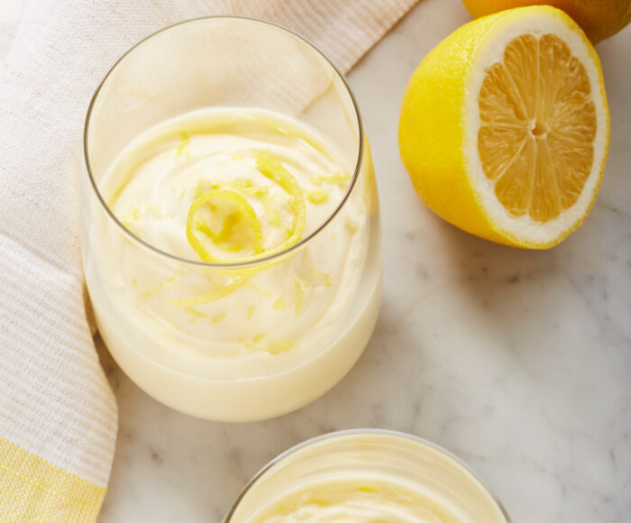 Two stemless wine glasses filled with lemon puree garnished with lemon zest.