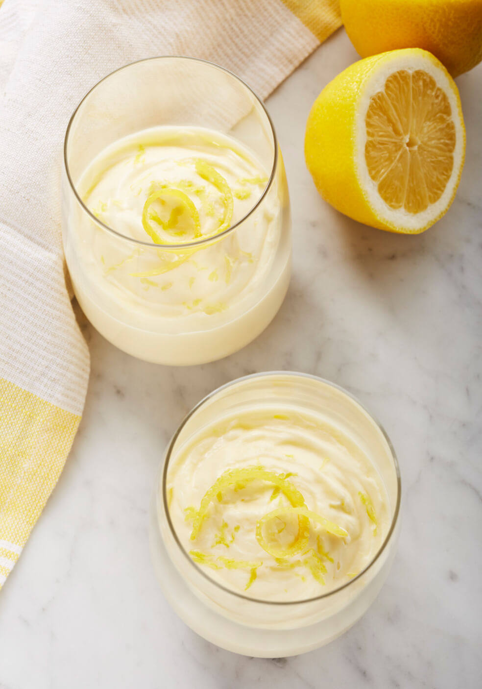 Two stemless wine glasses filled with lemon puree garnished with lemon zest.