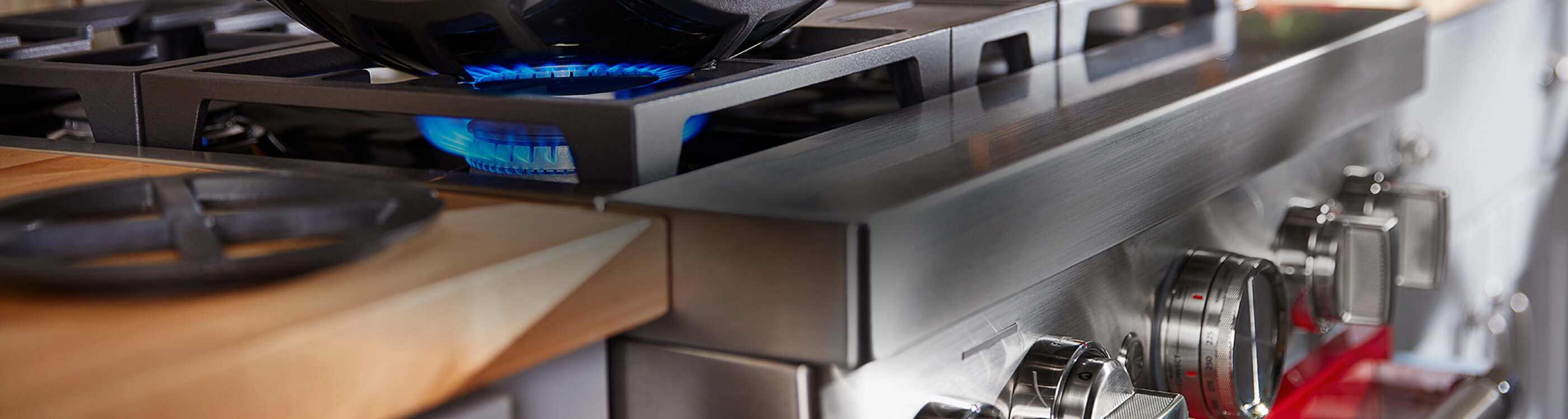 Close-up of commercial-style range, its handles, while a burner's flame heats a pot from below.