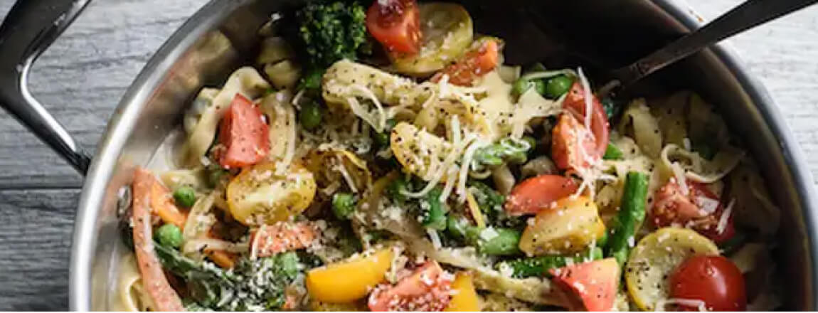 Pasta primavera in a bowl garnished with basil and parmesan cheese.