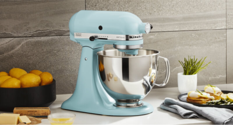 A blue KitchenAid® Stand Mixer on a countertop surrounded by different ingredients.