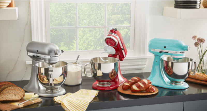 A trio of KitchenAid® Stand Mixers on a countertop with fresh baked bread on plates.