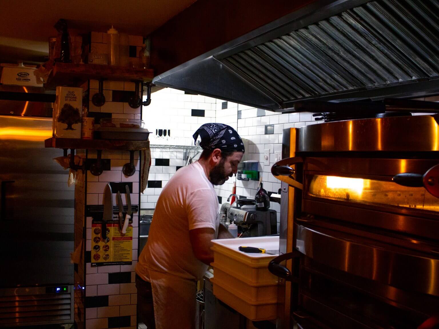 A man standing in his restaurant's kitchen working diligently over a pizza.