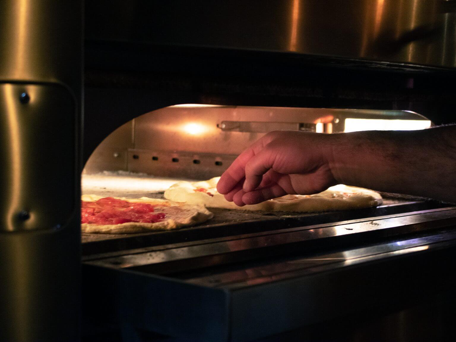 Two freshly made pizzas resting in a stainless steel pizza oven.