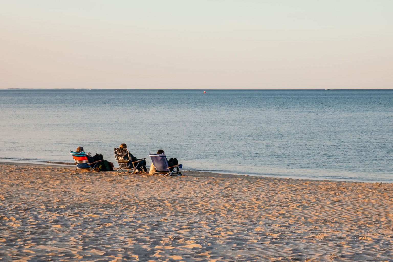 Three people relaxing in folding chairs on Crain's Beach.