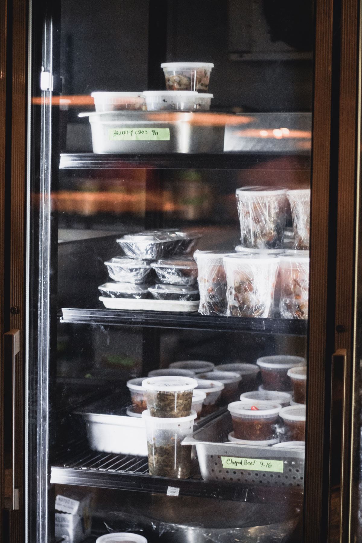 A refrigerator filled with containers of assorted meats, briskets and other eats.