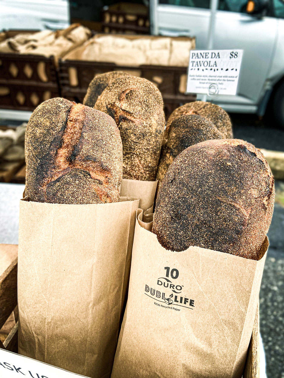 Four loaves of baked bread resting in individual brown paper bags.