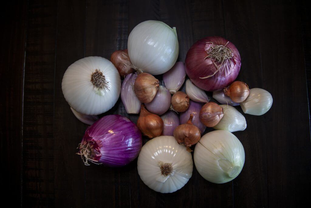 Assorted onions and shallots resting on a dark table.