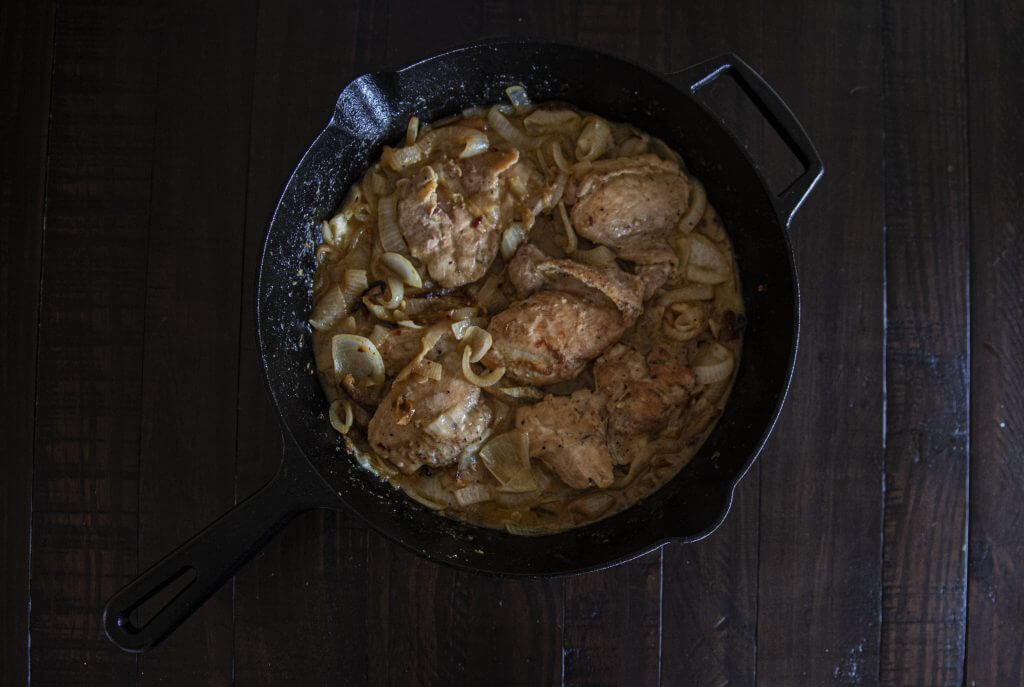 A cast iron skillet holding chicken thighs and caramelized onions.