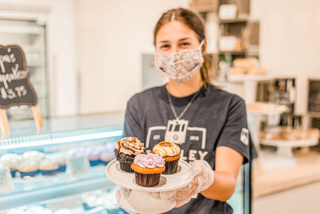 A person holding a small plate with three cupcakes.