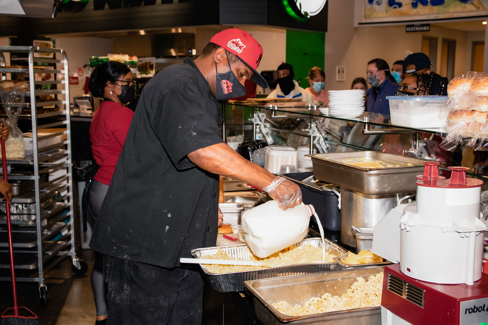 Sley adding milk to a large tray of mac and cheese.