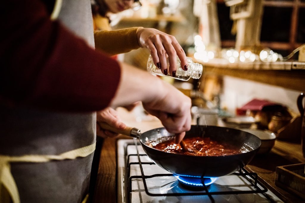 Two people cooking together as they prep sauce over the stove.