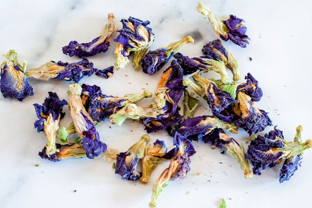 Dried butterfly pea flower petals scattered on a white table.