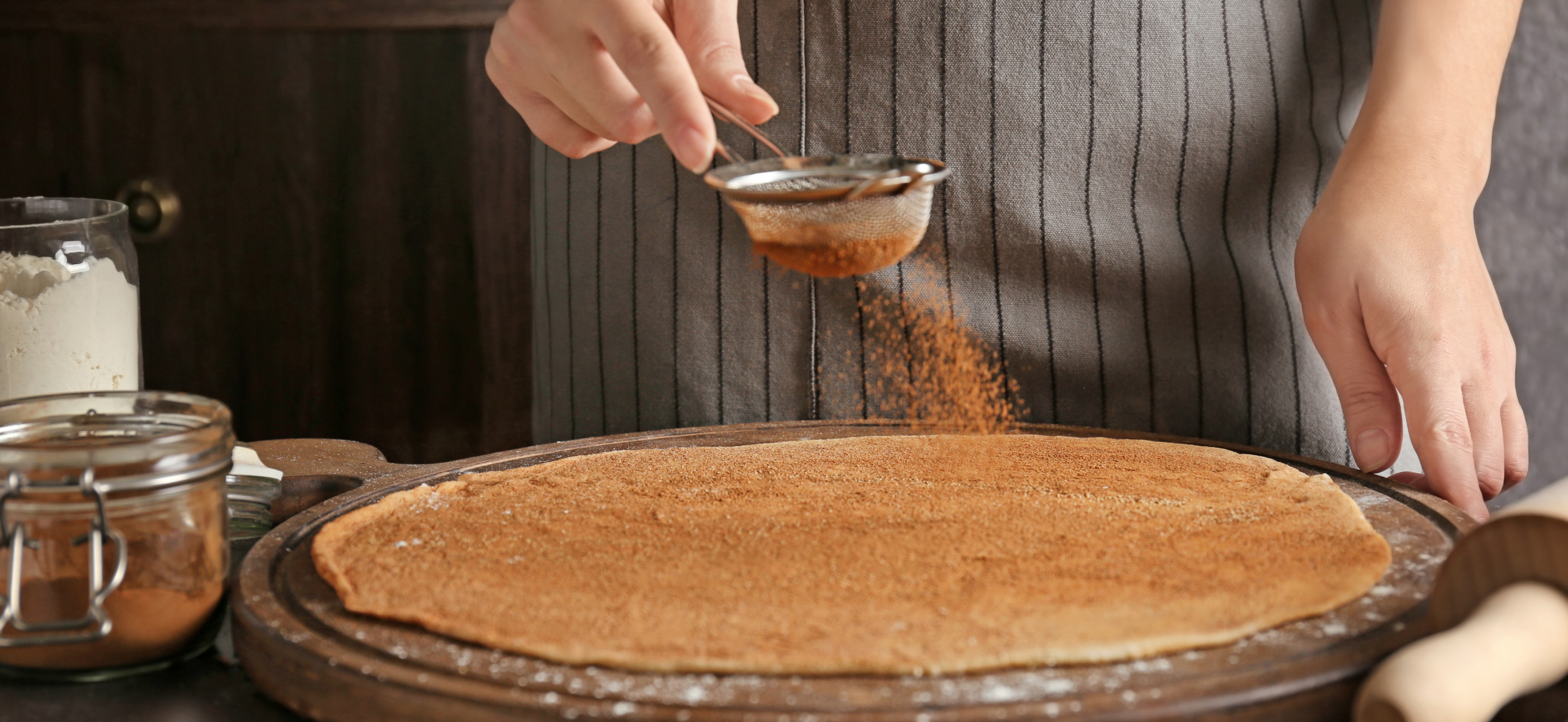Person dusting dough with sifted cinnamon 