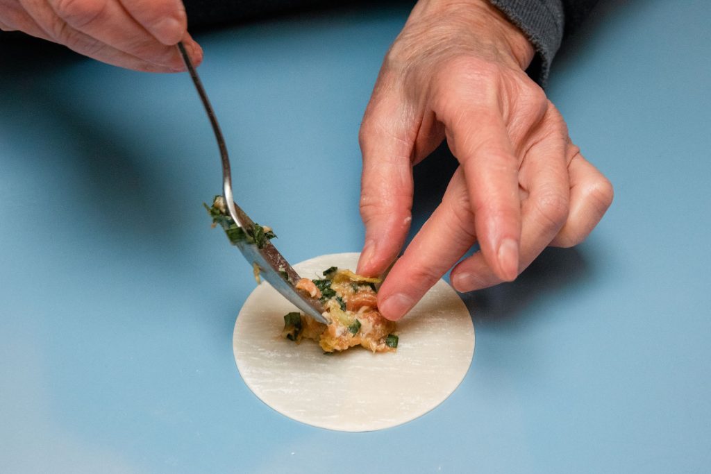 A person gently placing filling into a dumpling wrapper.