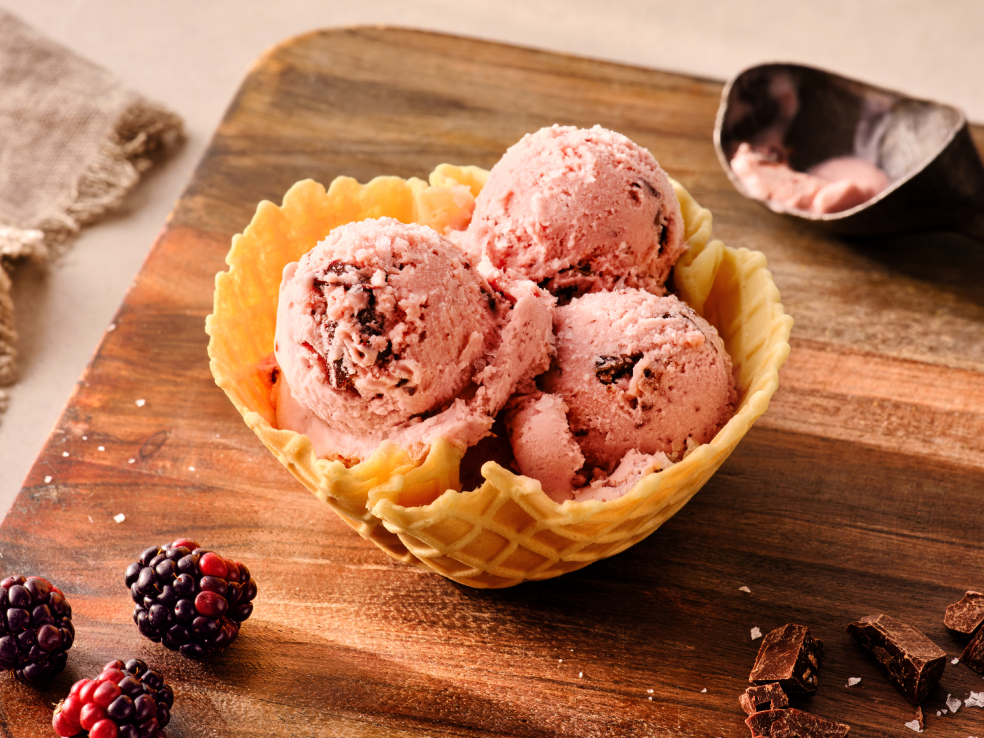 Several scoops of pink blackberry ice cream in a waffle cone bowl.