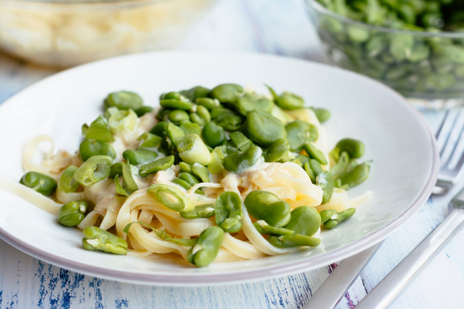 A white dish of spaghetti topped with fava beans.