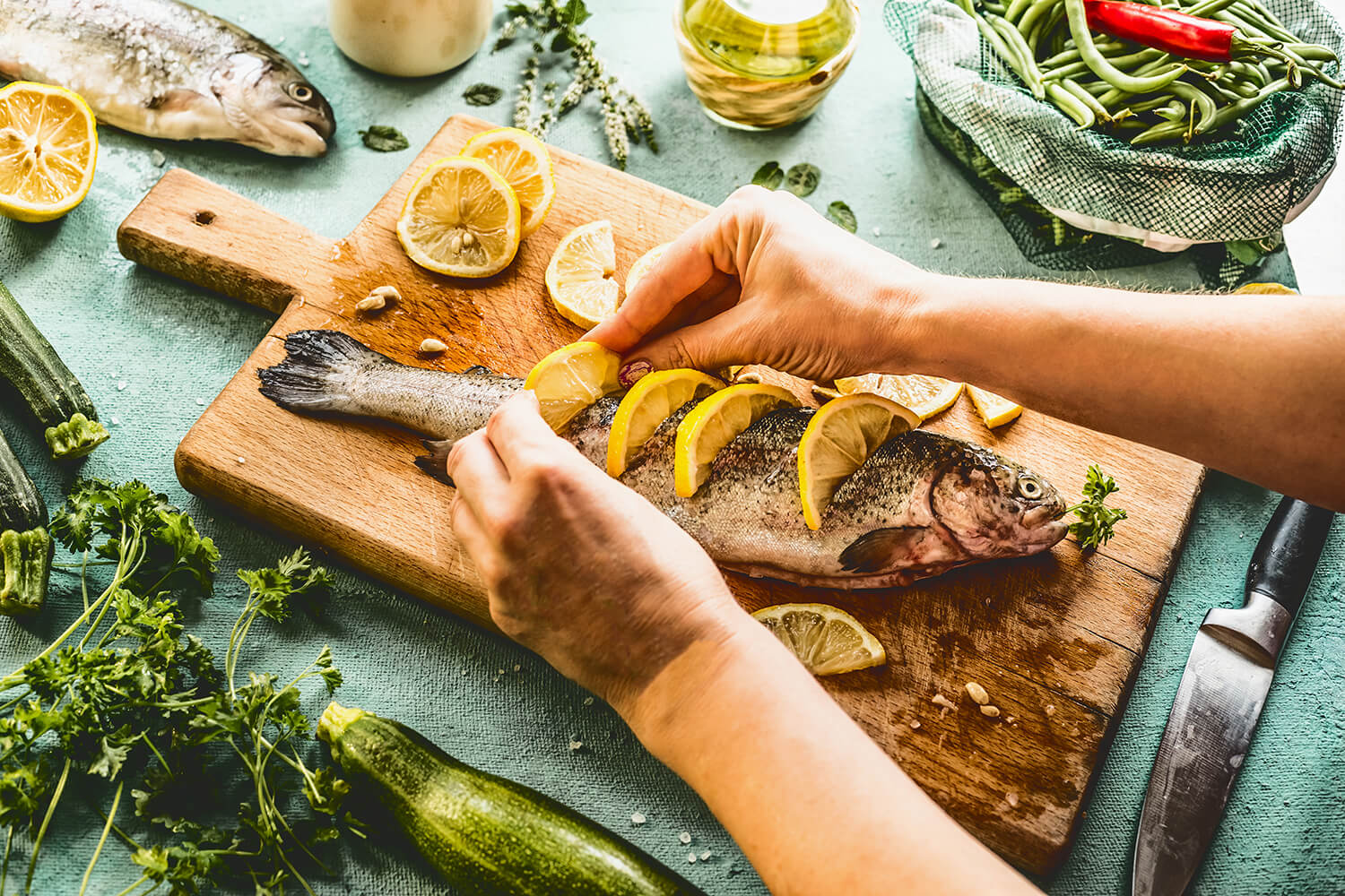A whole fish laid down on a rustic wooden cutting board garnished with sliced lemons.