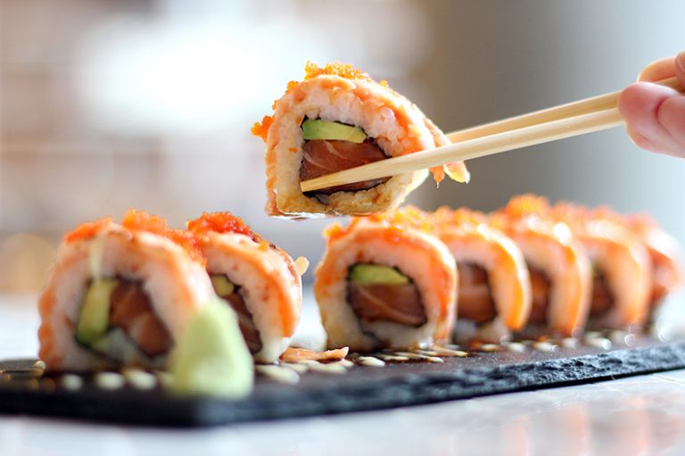 Wooden chopsticks lifting up a single, delicate roll of sushi.