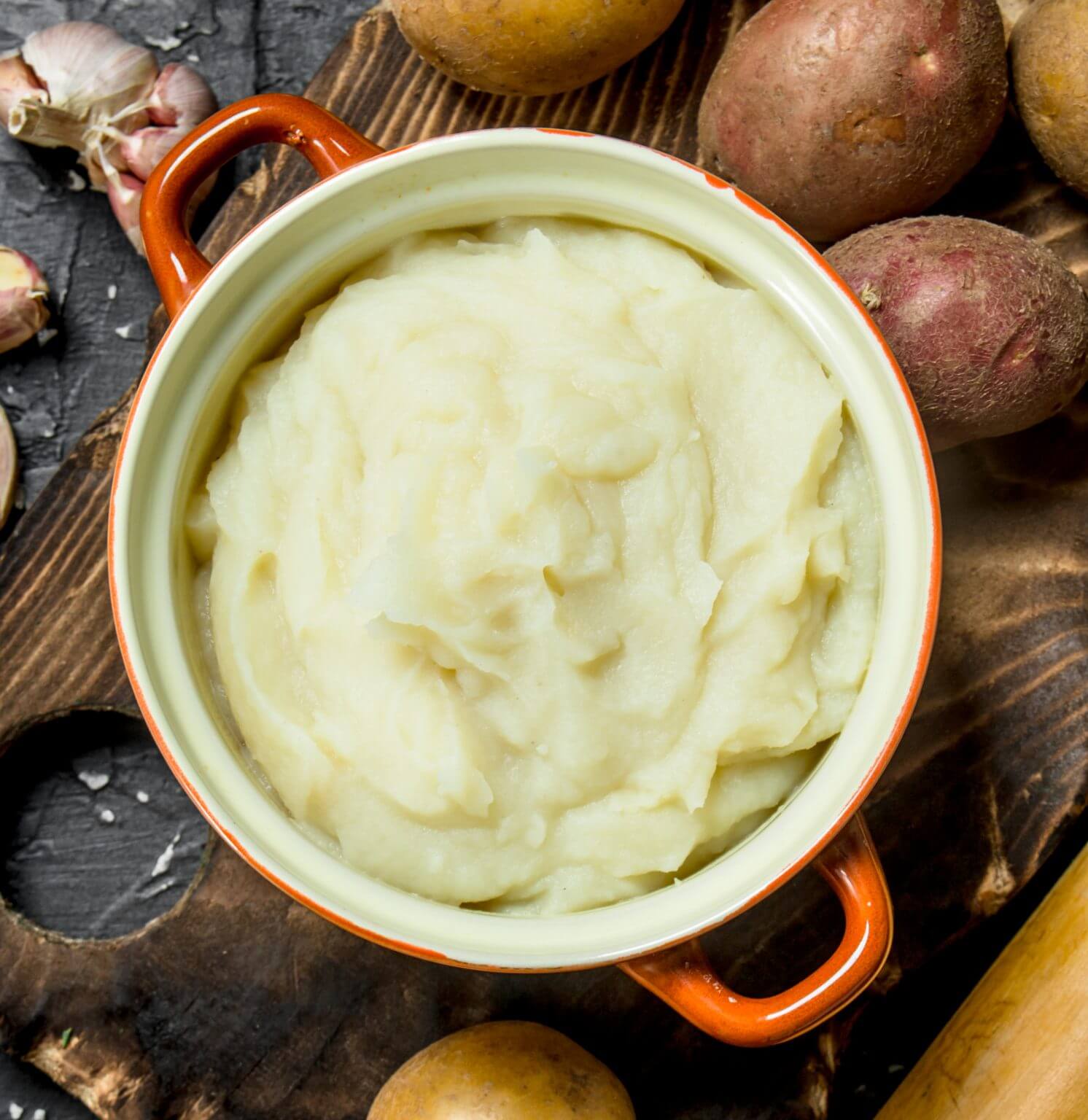 An orange dutch oven resting on a wooden cutting board filled with whipped potatoes.